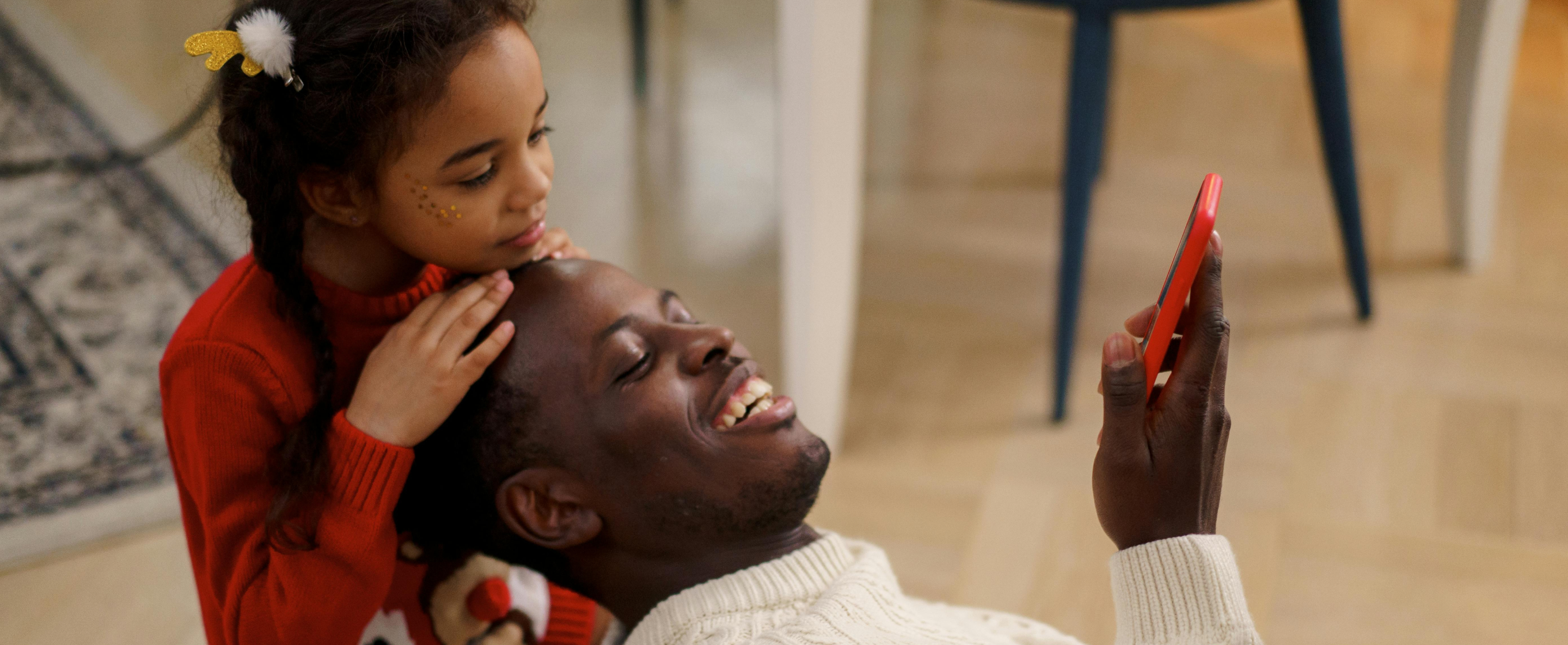 a father and daughter relax in a living room while watching a mobile device